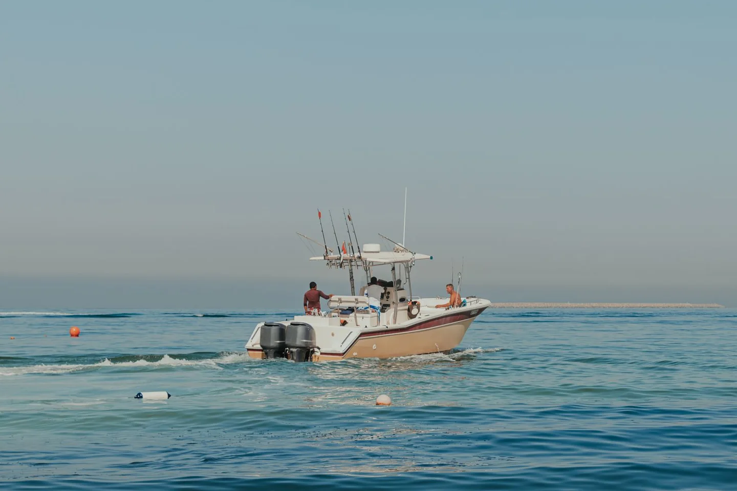 A center-console fishing boat with a T-top and twin outboard motors cruising on blue coastal water